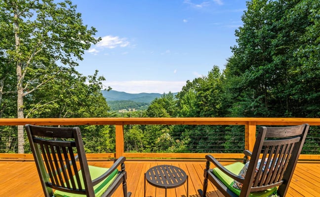 Wooden deck with two rocking chairs overlooking forested mountains and valley under clear blue sky